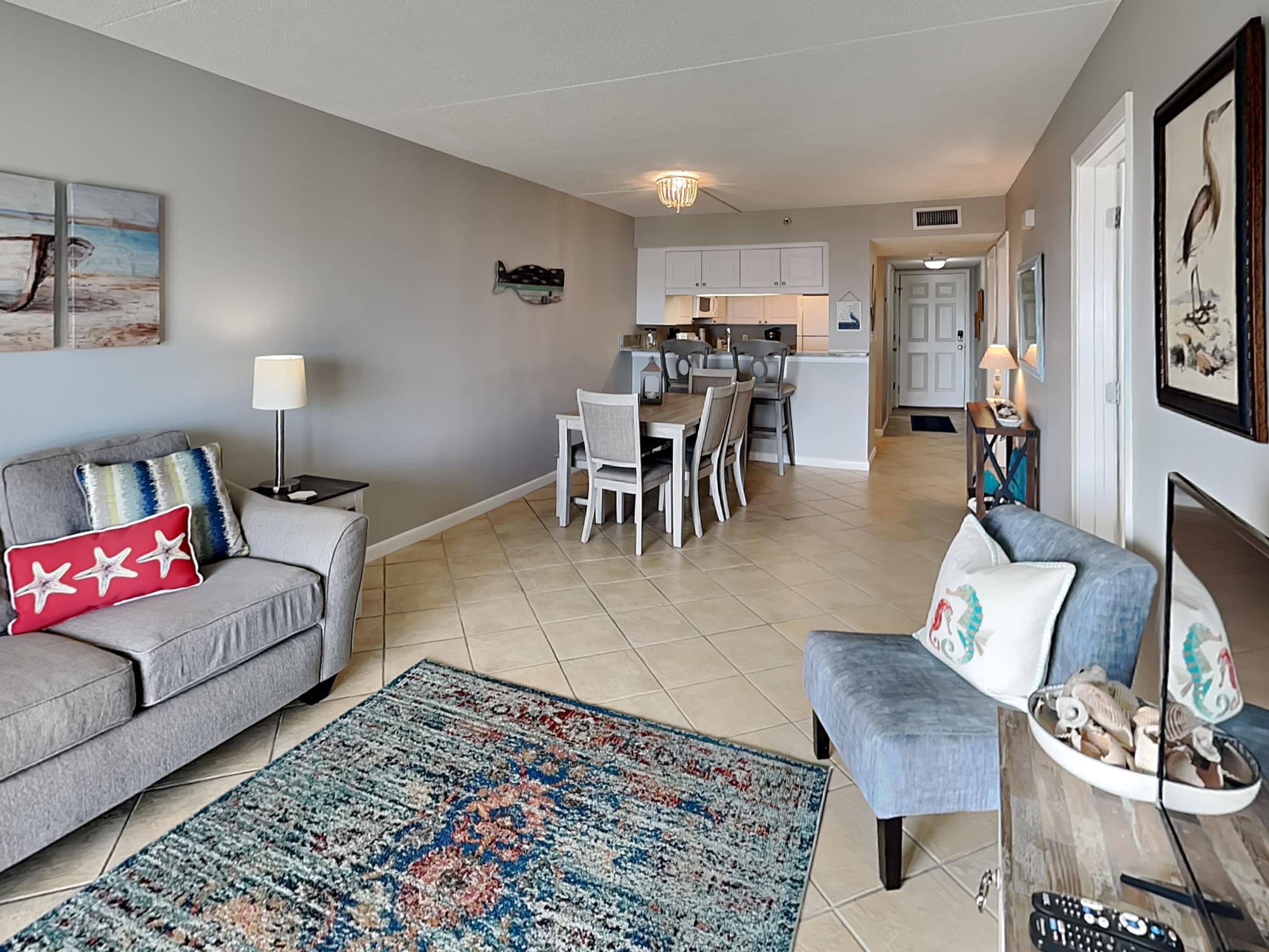 A living room with a grey sofa, a patterned rug, and a dining area with a kitchen in the background.