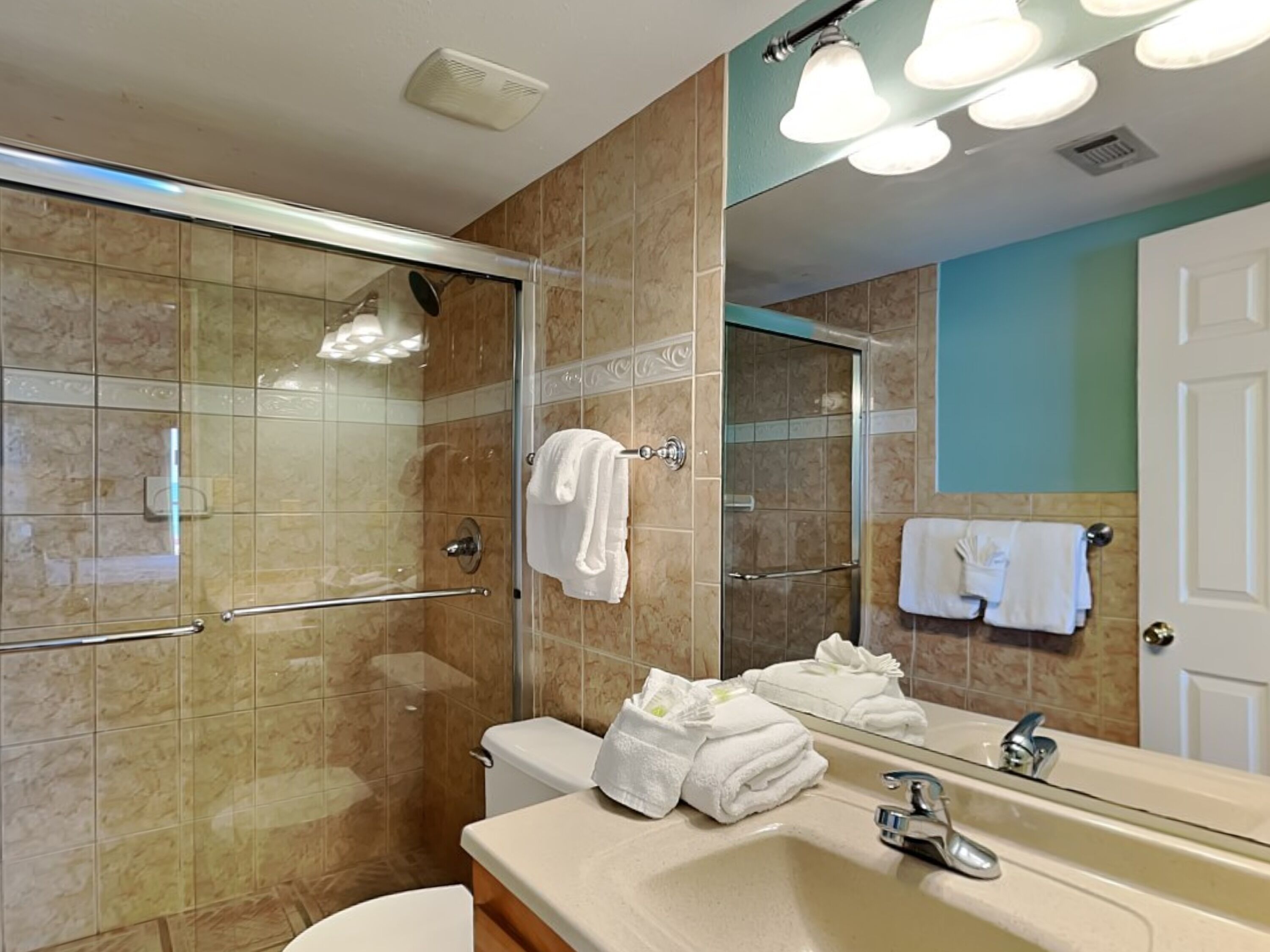 A modern bathroom with a glass-enclosed shower, a vanity with a sink and mirror, and towels on the wall.