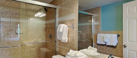 A modern bathroom with a glass-enclosed shower, a vanity with a sink and mirror, and towels on the wall.