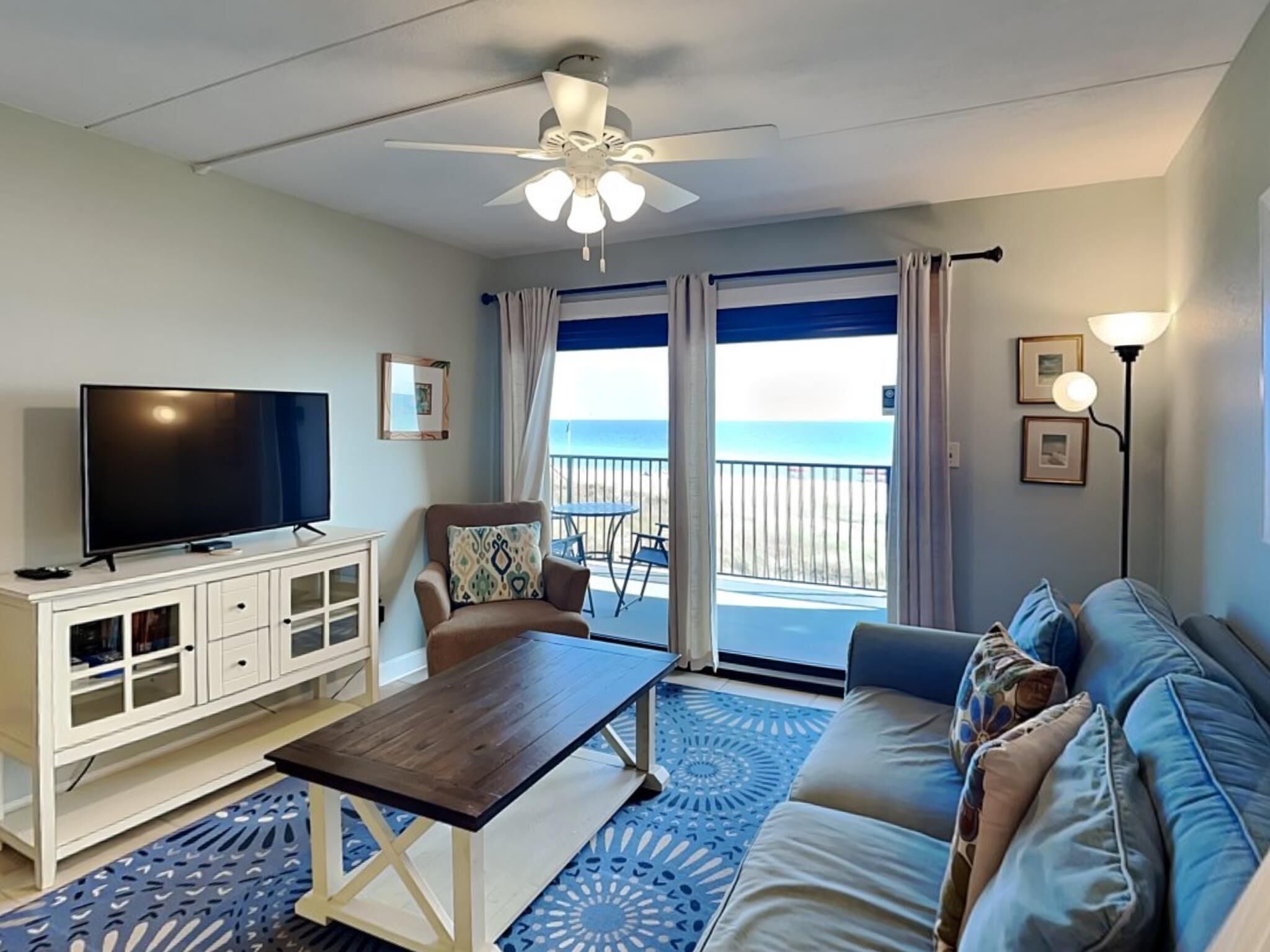 A living room with a TV, a sofa, a coffee table, and a balcony with a view of the beach.
