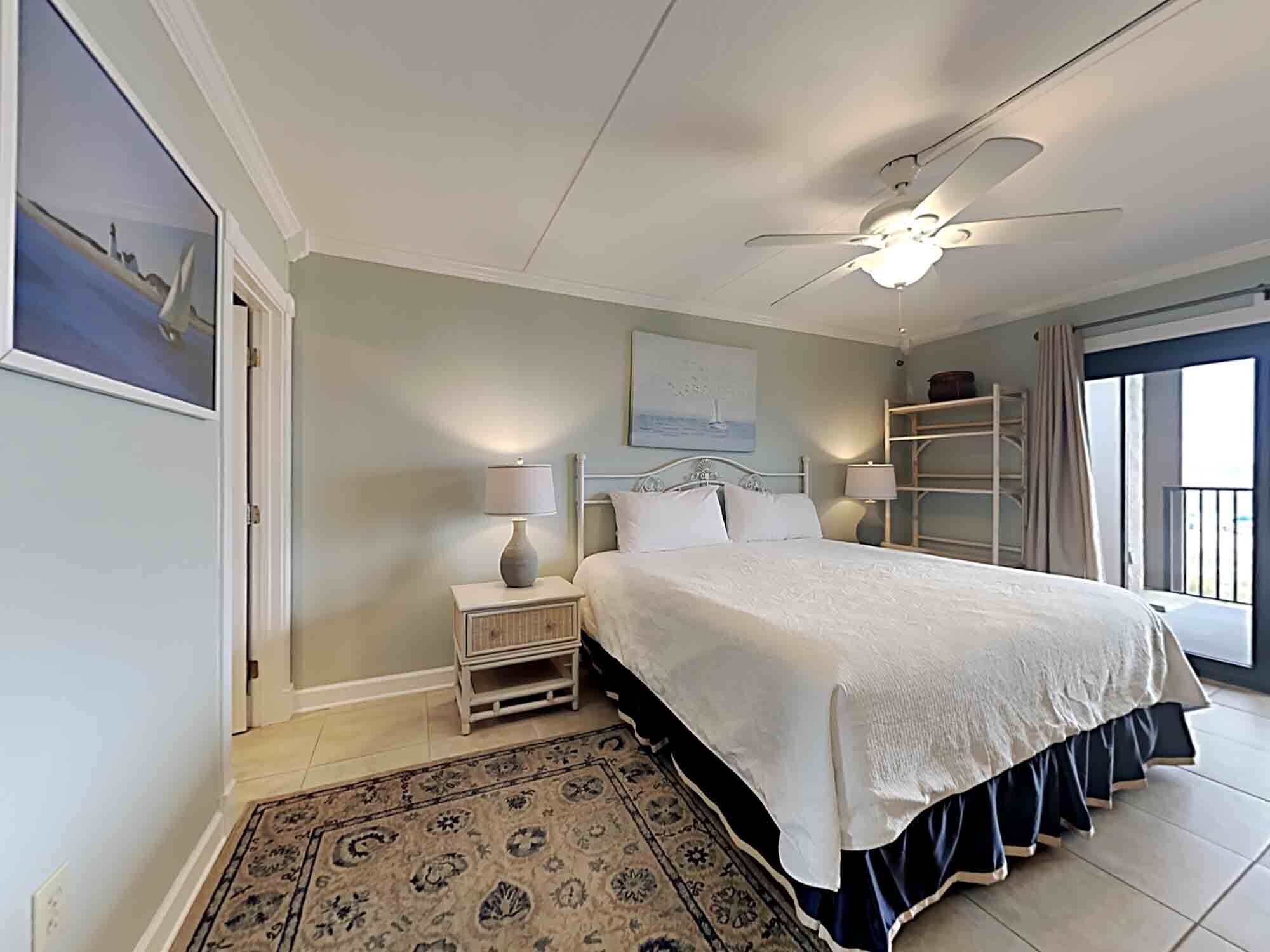 A bedroom with a bed, nightstands, a ceiling fan, a window with curtains, and a view of the outside.