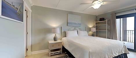 A bedroom with a bed, nightstands, a ceiling fan, a window with curtains, and a view of the outside.