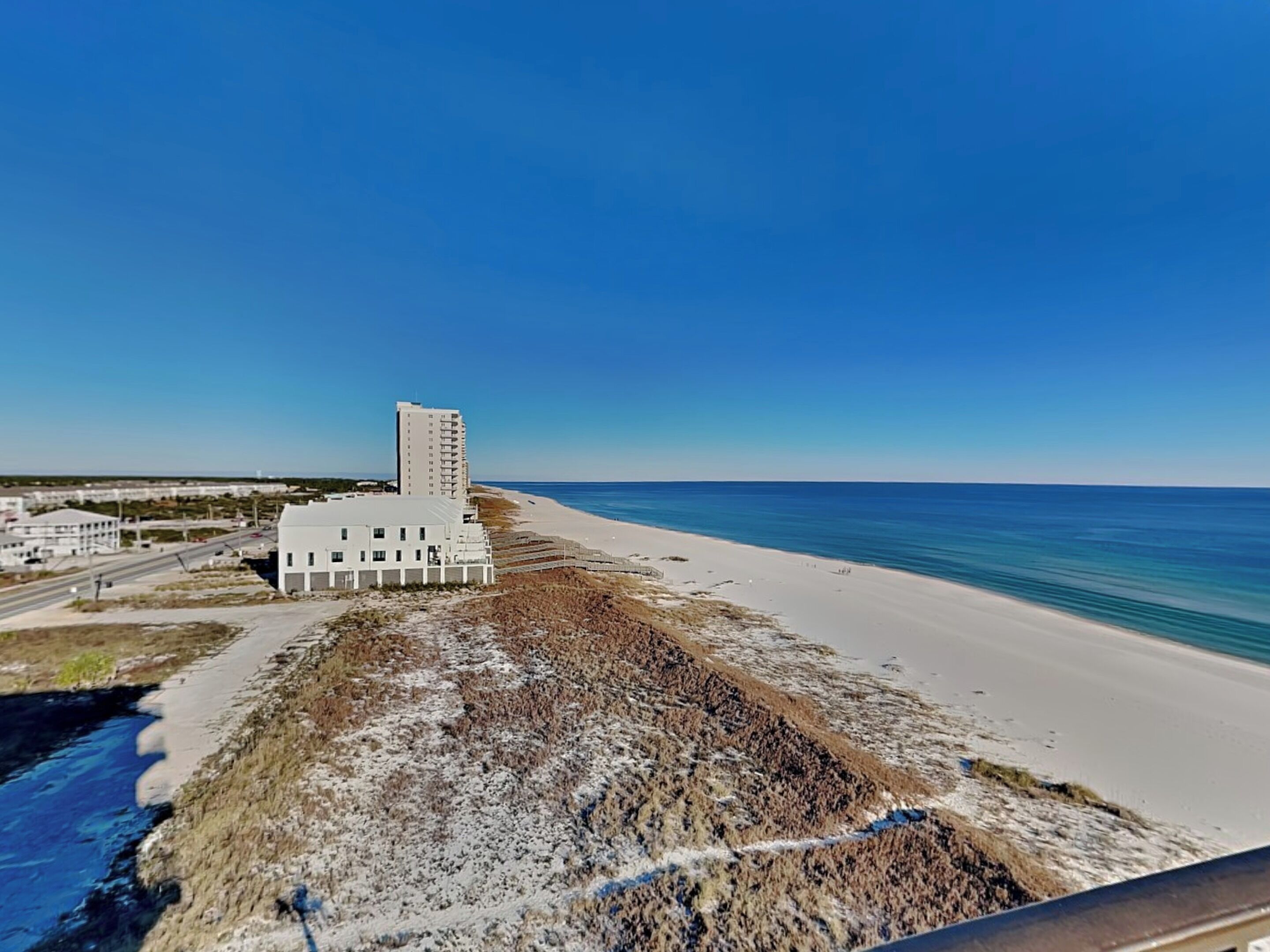 A coastal hotel with a beach view, a parking area, and a road leading to the beach.