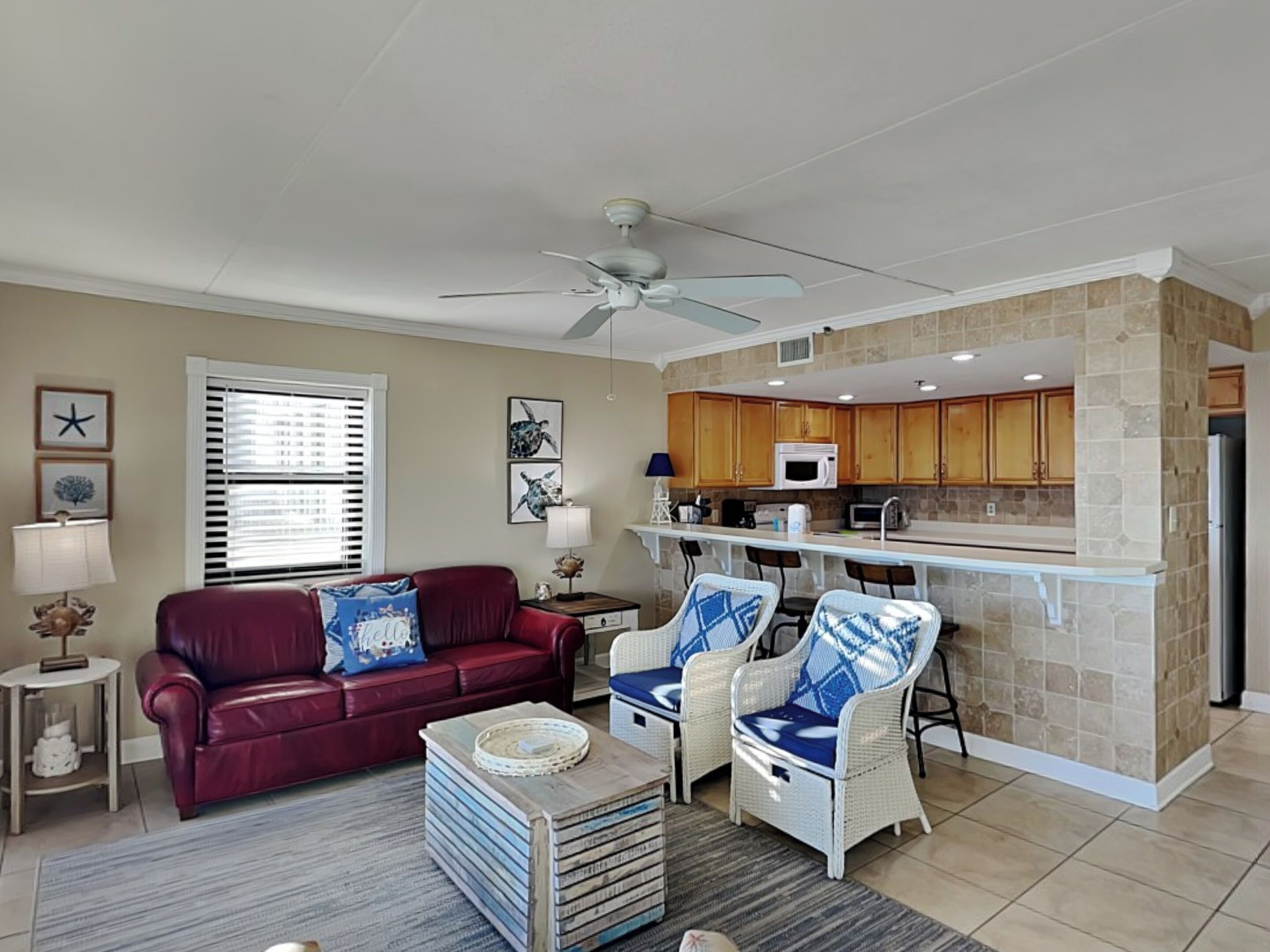 A living room with a red sofa, a coffee table, and a kitchen area with a microwave and wooden cabinets.