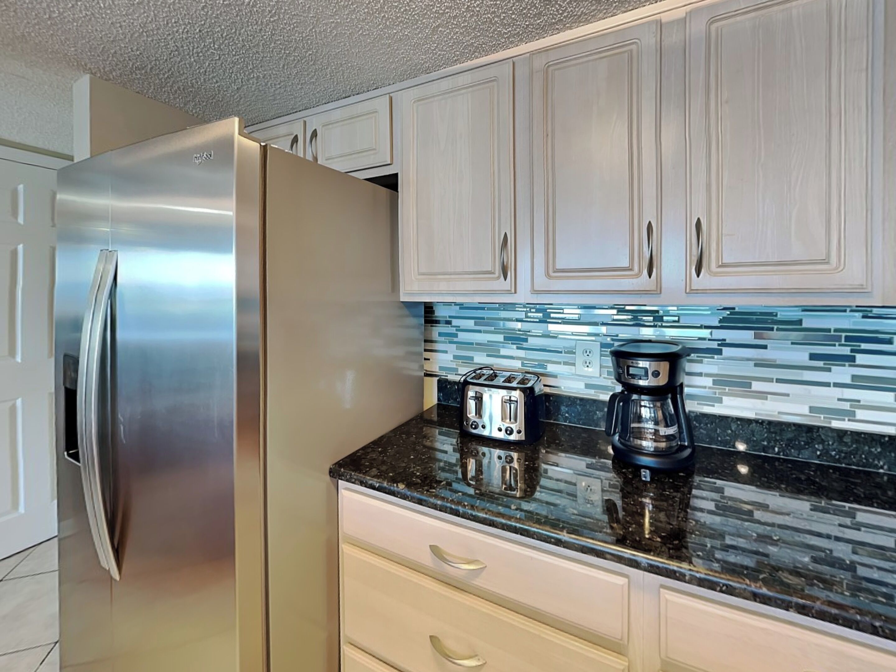 A kitchen with a stainless steel refrigerator, a toaster, and a coffee maker on the counter.