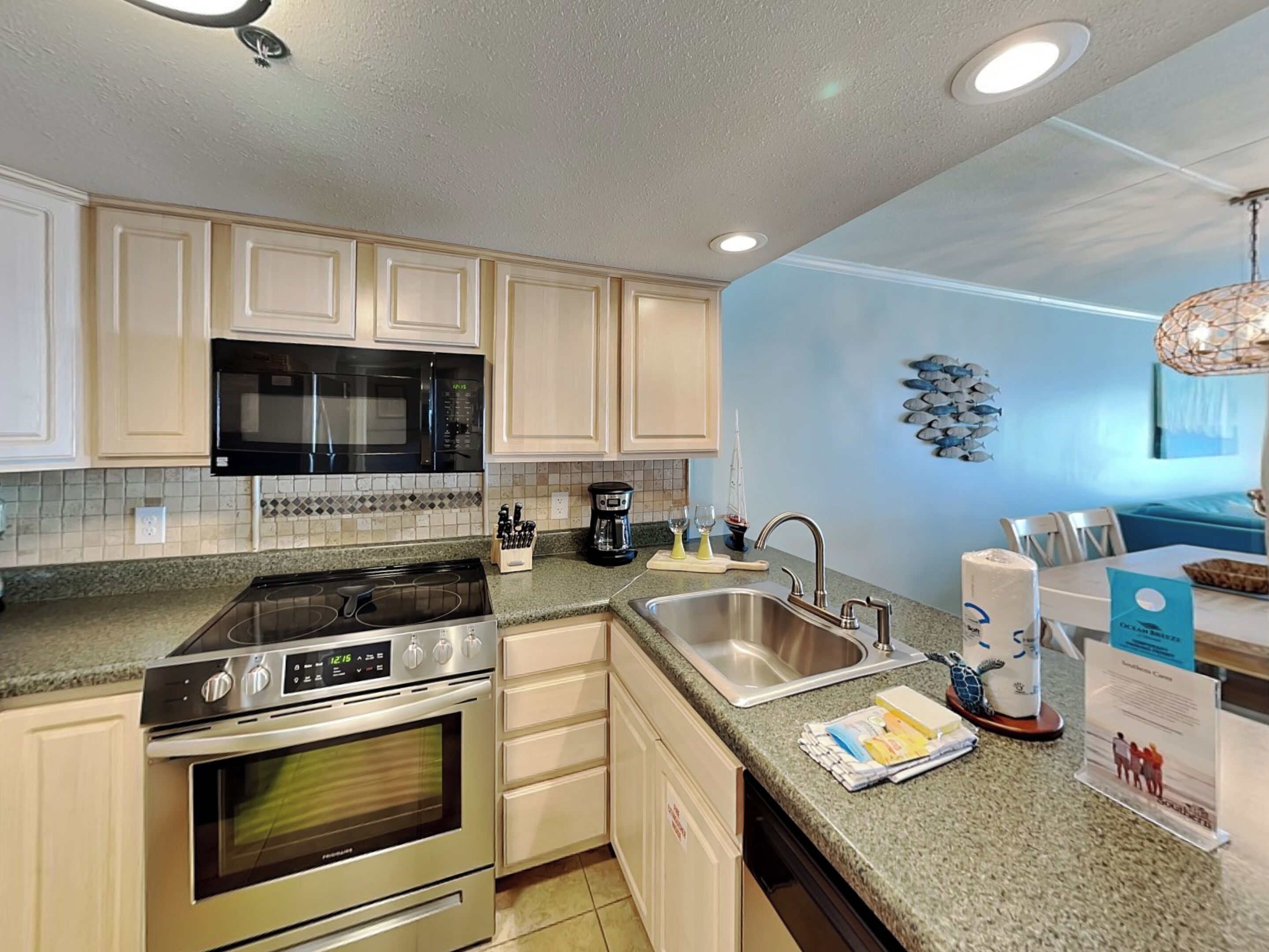 A modern kitchen with stainless steel appliances, a granite countertop, and a view of the ocean through the window.