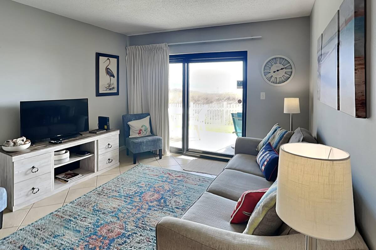A modern living room with a flat-screen TV, a sofa, a coffee table, and a large window with curtains.