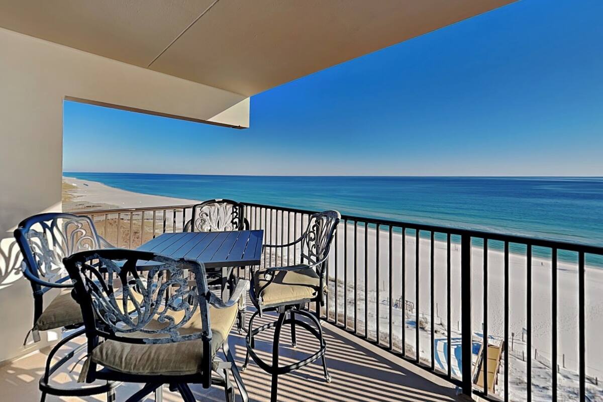 A balcony with a table and chairs overlooking a beach.