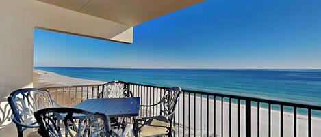A balcony with a table and chairs overlooking a beach.