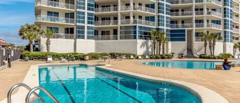 A multi-story hotel with a swimming pool, palm trees, and a clear blue sky.