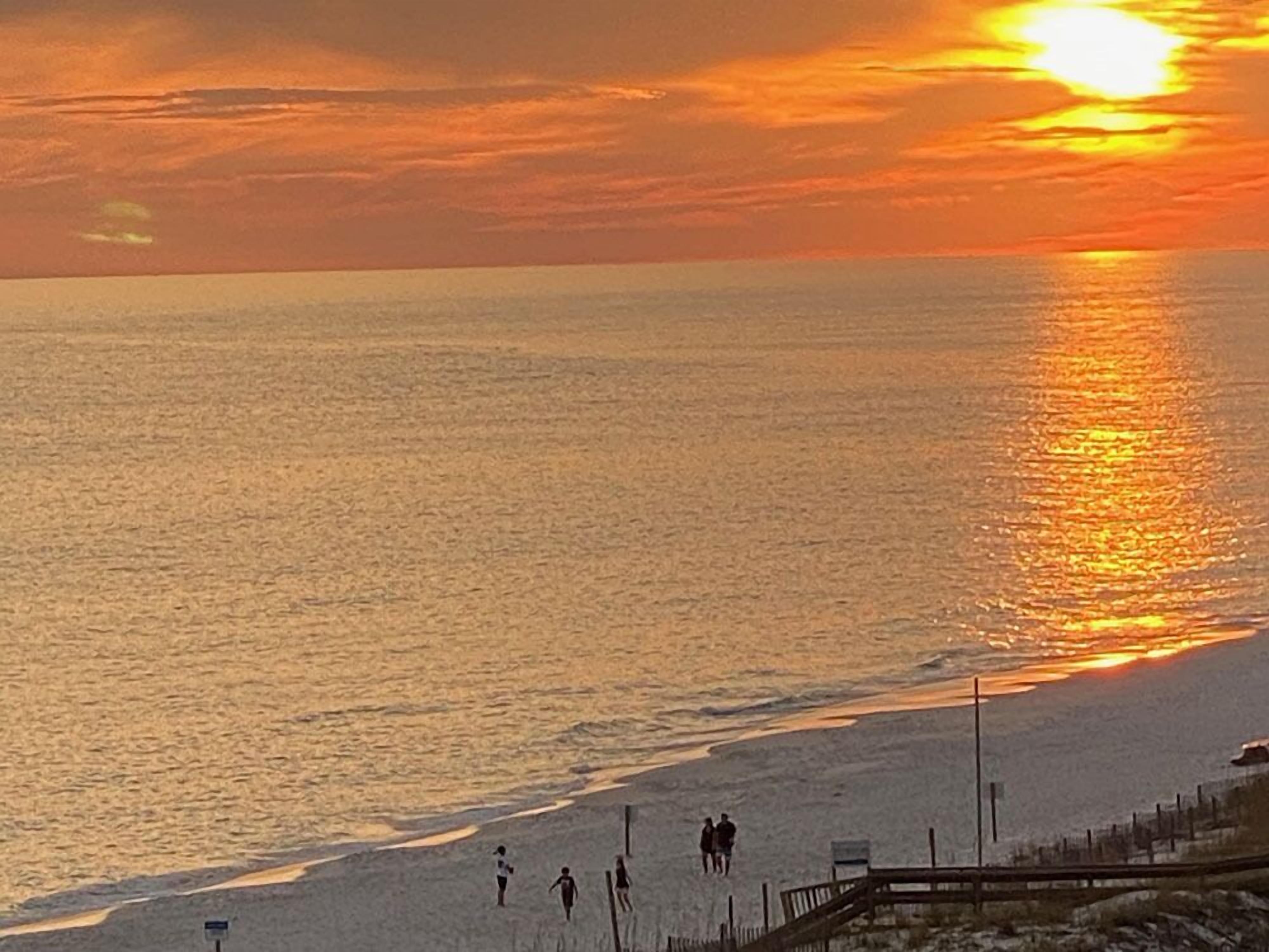 Un coucher de soleil sur une plage, avec des personnes se promenant le long du rivage.