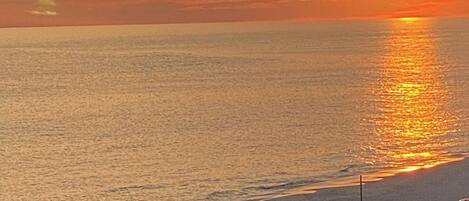 Un coucher de soleil sur une plage, avec des personnes se promenant le long du rivage.
