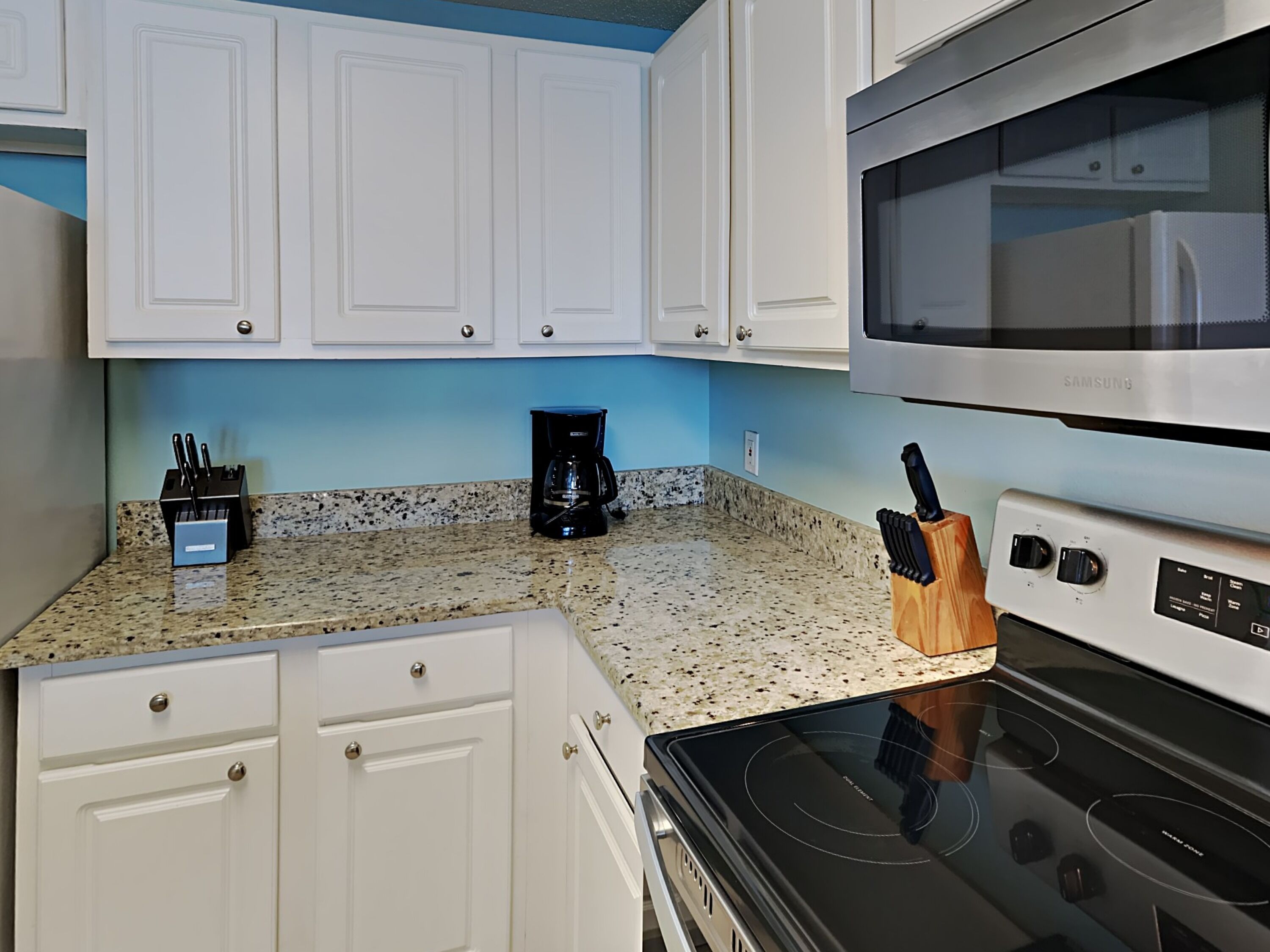 A kitchen with white cabinets, a stainless steel microwave, a black coffee maker, and a knife block.