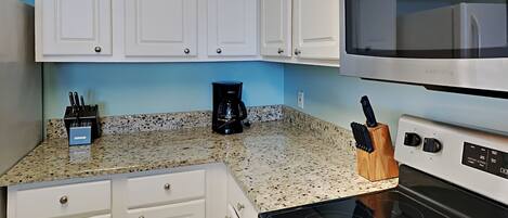 A kitchen with white cabinets, a stainless steel microwave, a black coffee maker, and a knife block.