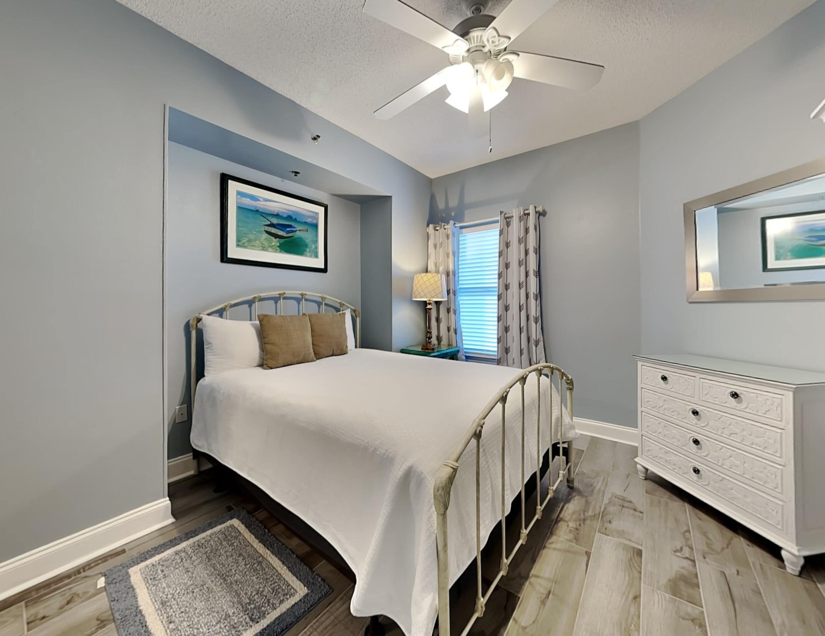 A bedroom with a bed, a nightstand, a dresser, a ceiling fan, and a window with curtains.