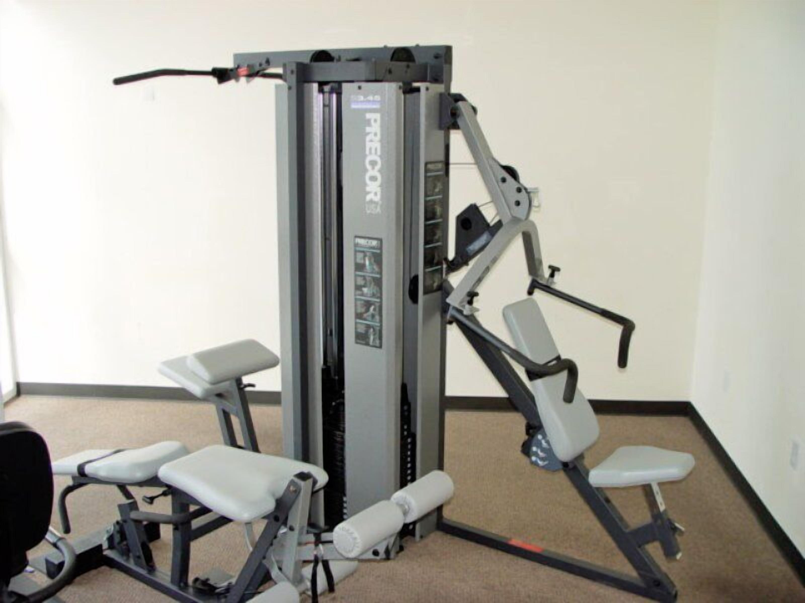A gym with a Precor machine, two benches, and a wall-mounted exercise station.