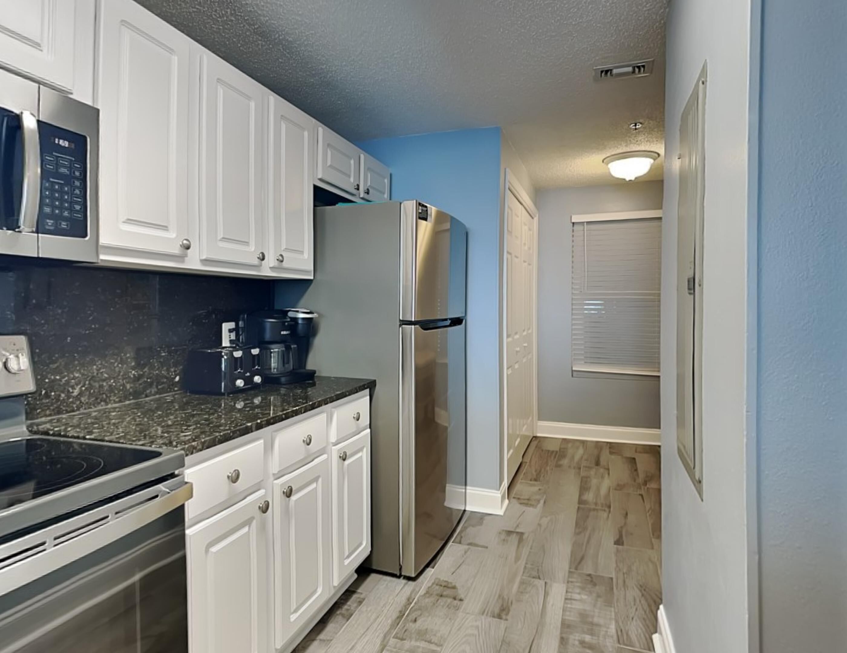 A compact kitchen with white cabinets, a stainless steel refrigerator, a coffee maker, and a microwave.