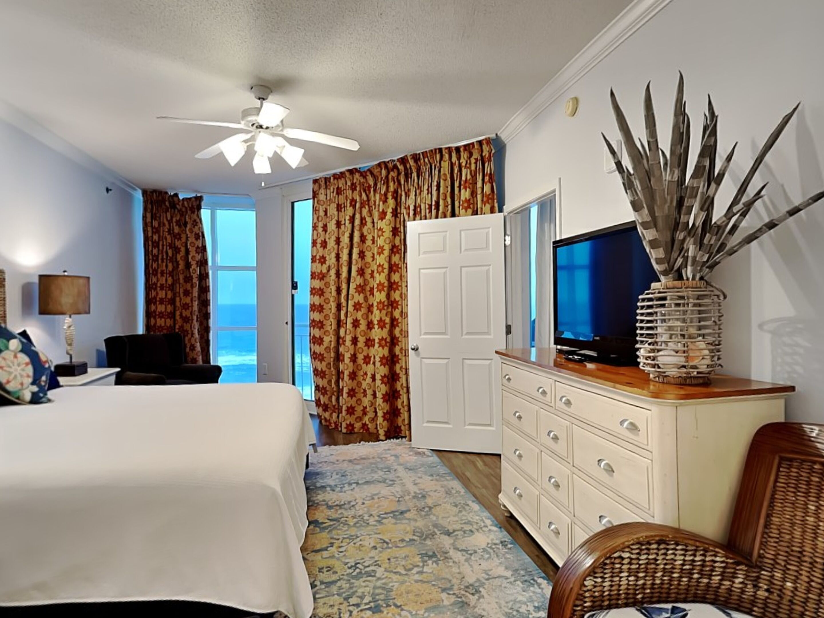 A hotel room with a bed, a television, a dresser, and a view of the ocean.