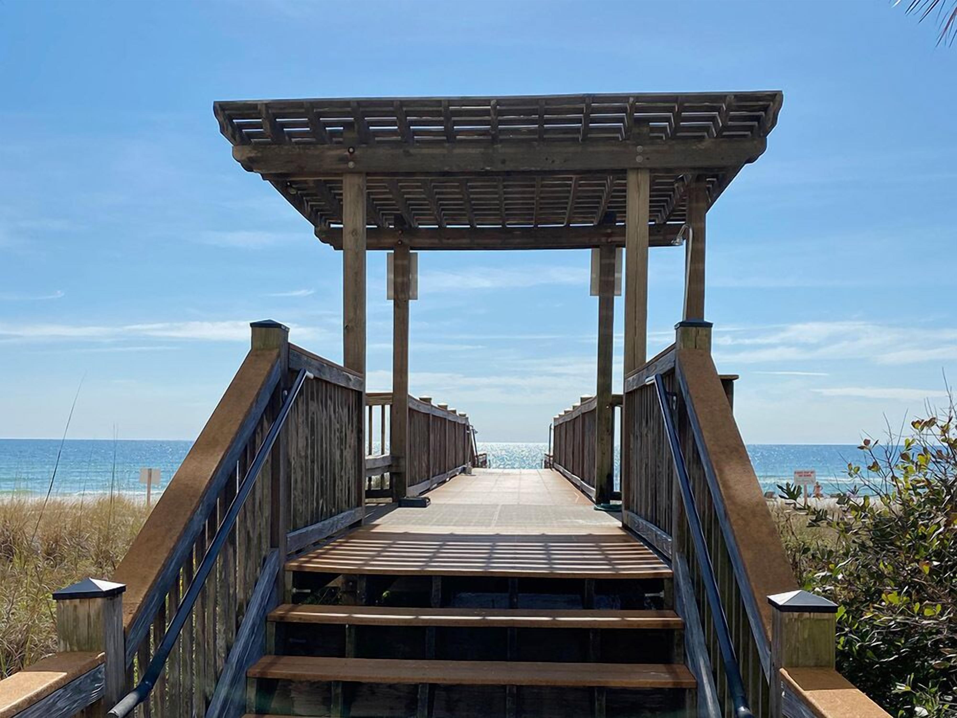 Een houten looppad dat leidt naar een overdekte kiosk met uitzicht op de oceaan.