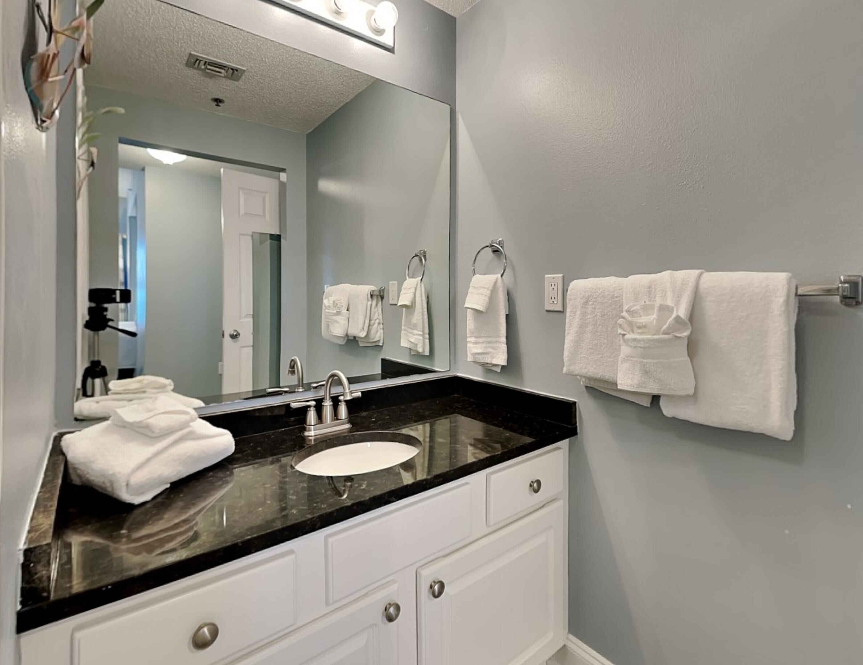 A bathroom with a black countertop sink, white cabinets, and a large mirror.