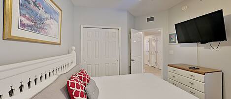A bedroom with a bed, a ceiling fan, a TV, and a door leading to another room.