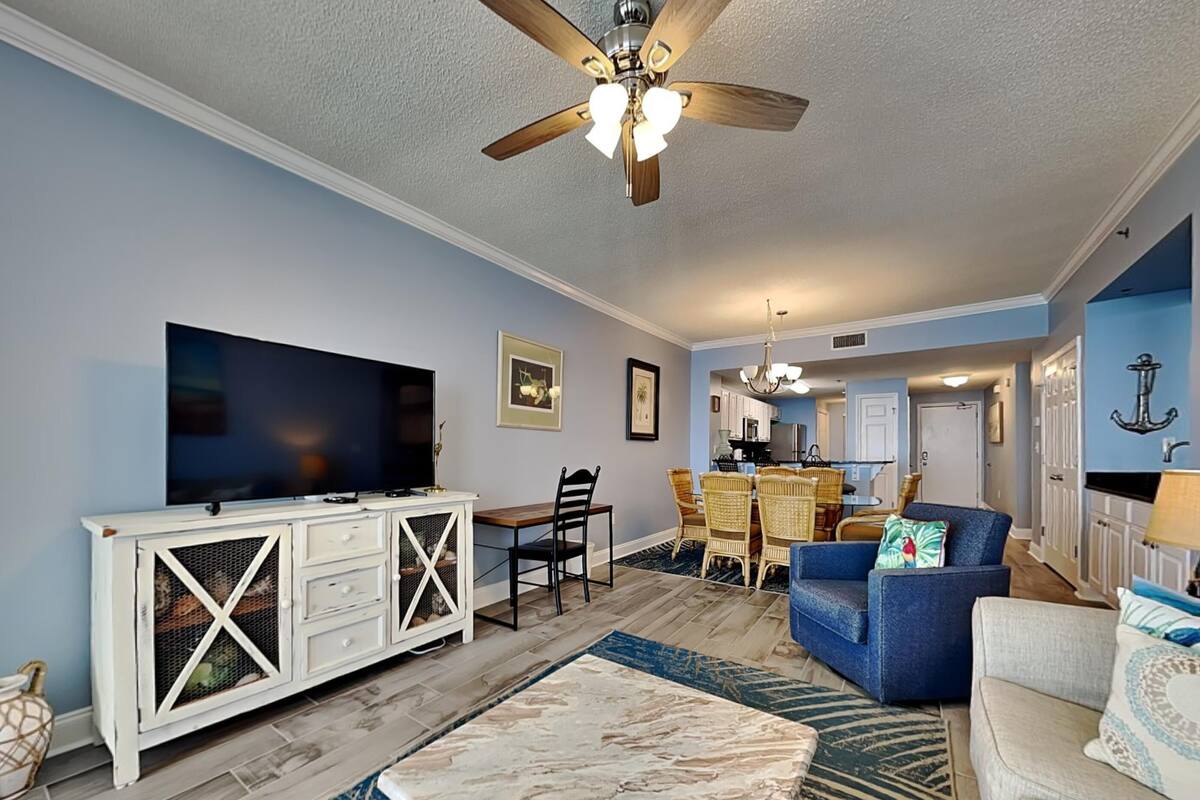 A living room with a TV, white cabinet, blue sofa, and a ceiling fan.