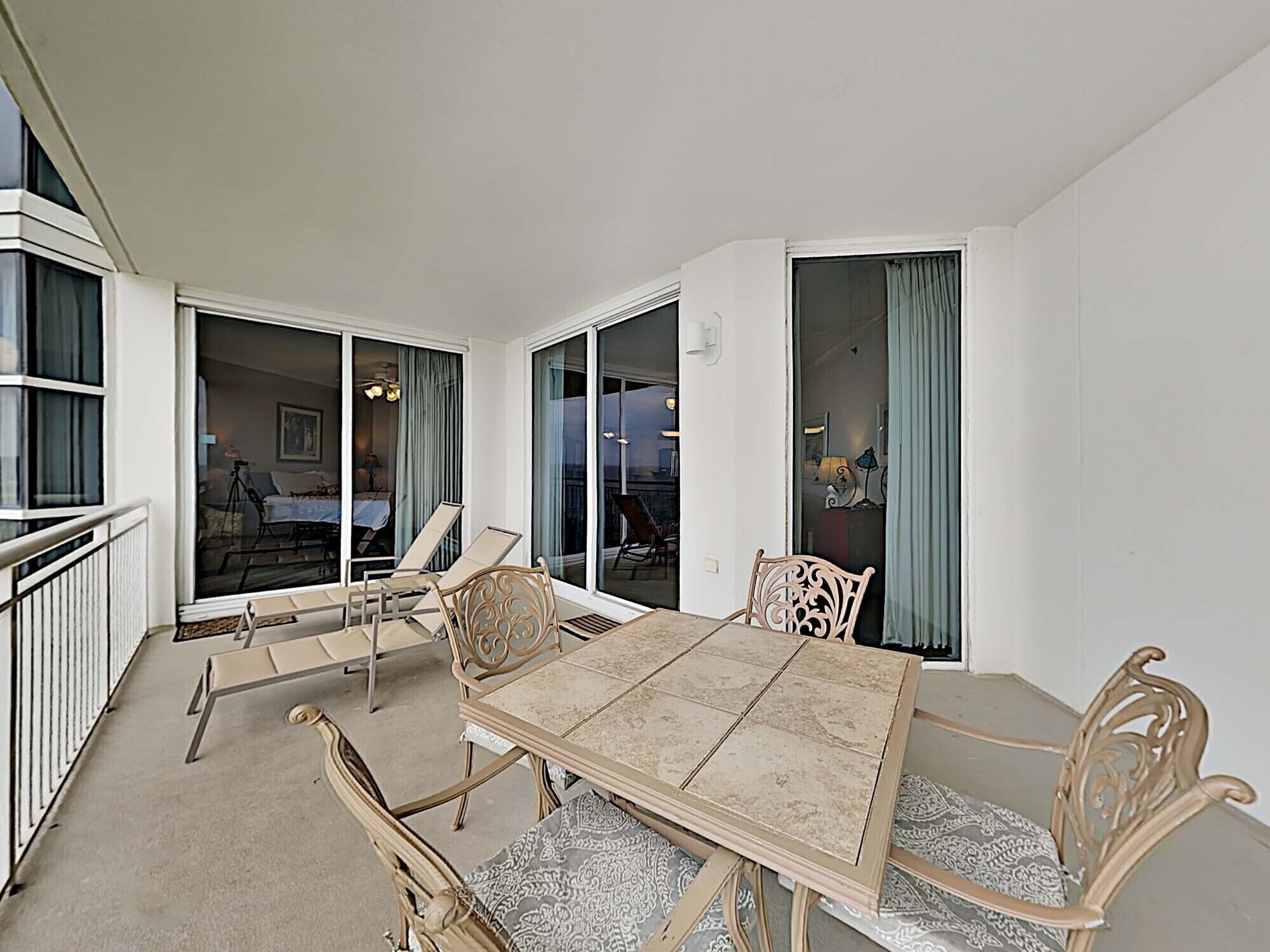 A spacious balcony with a dining table and chairs, large sliding glass doors leading to a living area, and a view of the outside.