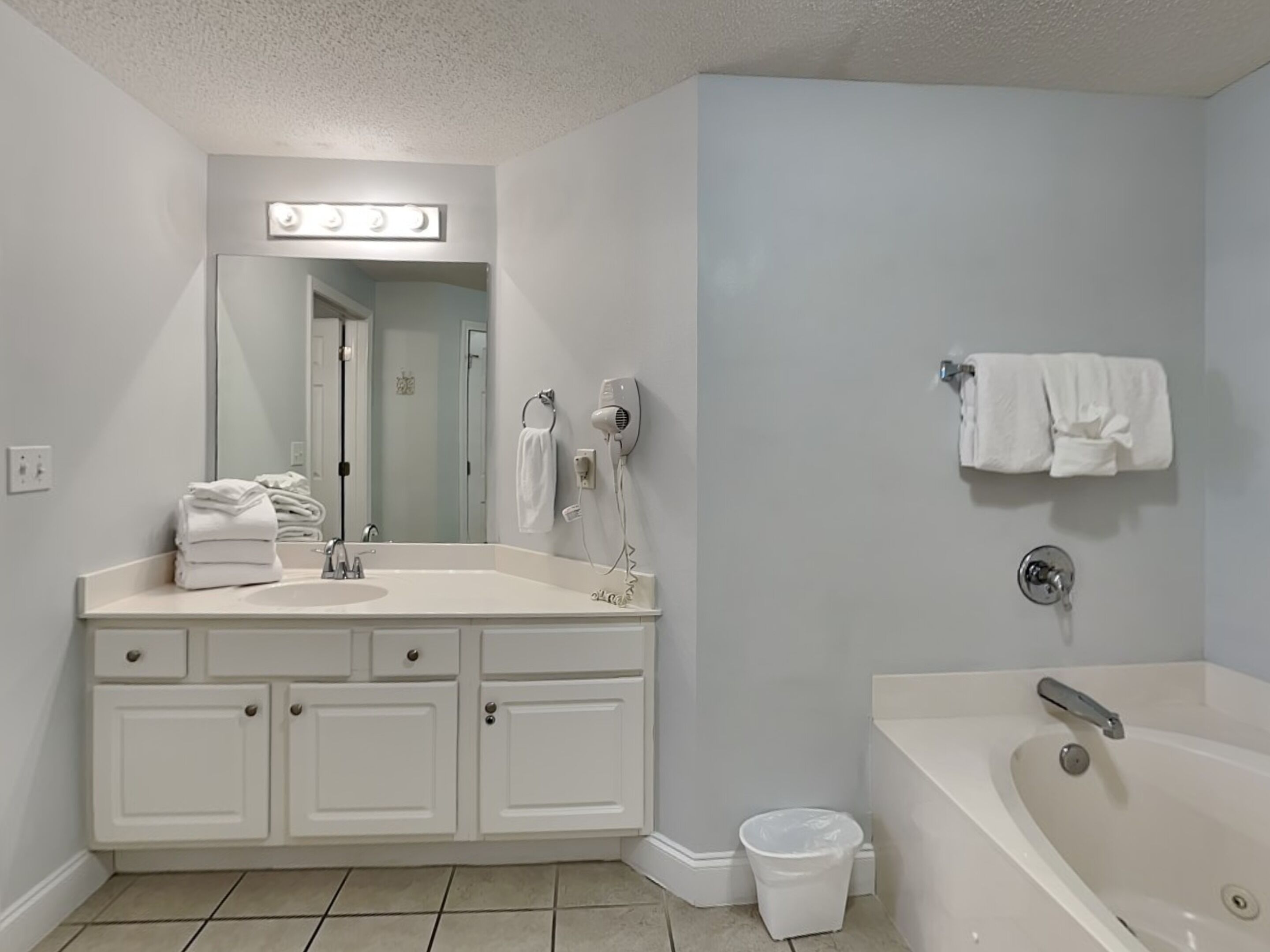 Une salle de bain moderne avec un meuble-lavabo blanc, un grand miroir, un sèche-cheveux et une baignoire.