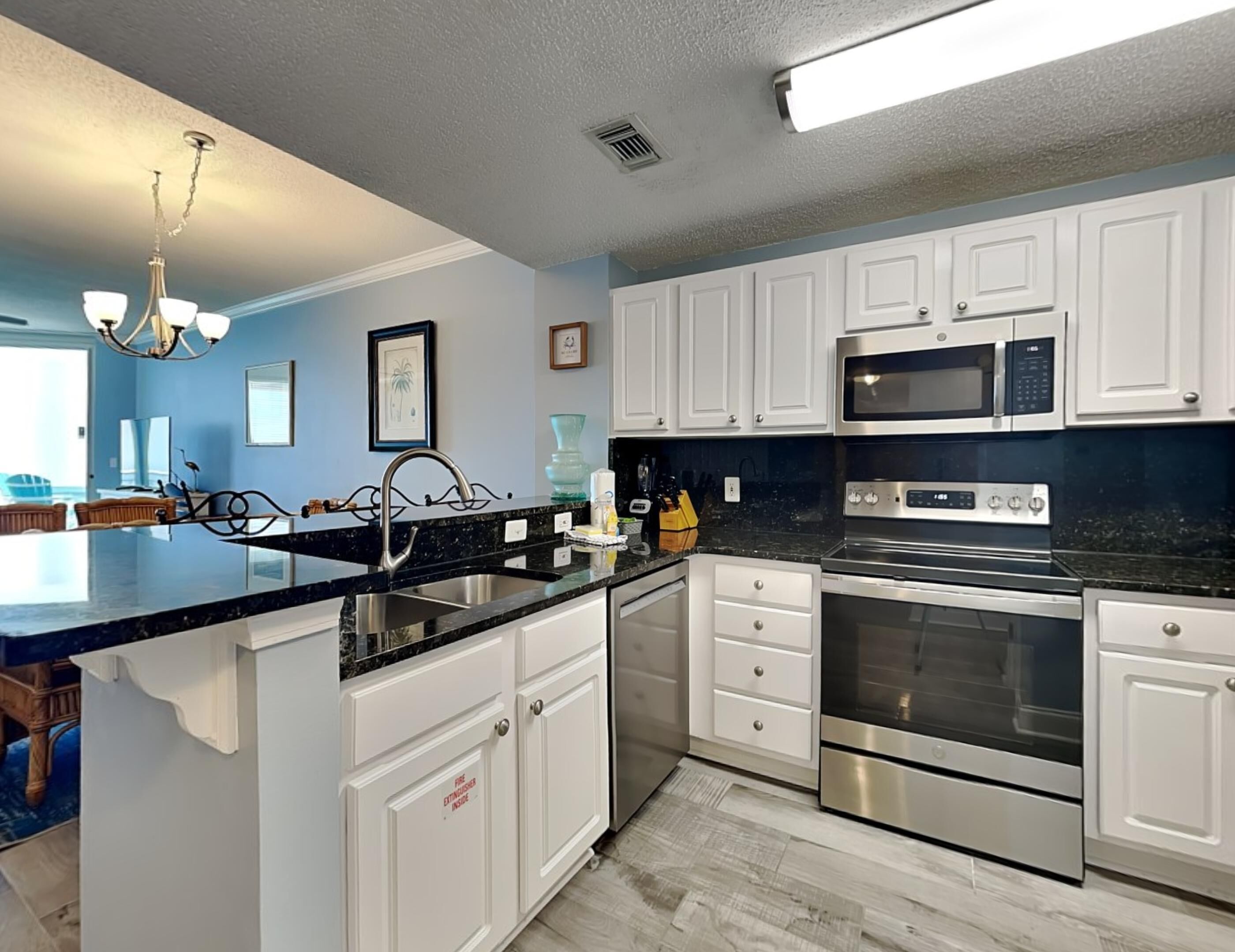 A modern kitchen with white cabinets, a black countertop, stainless steel appliances, and a chandelier.