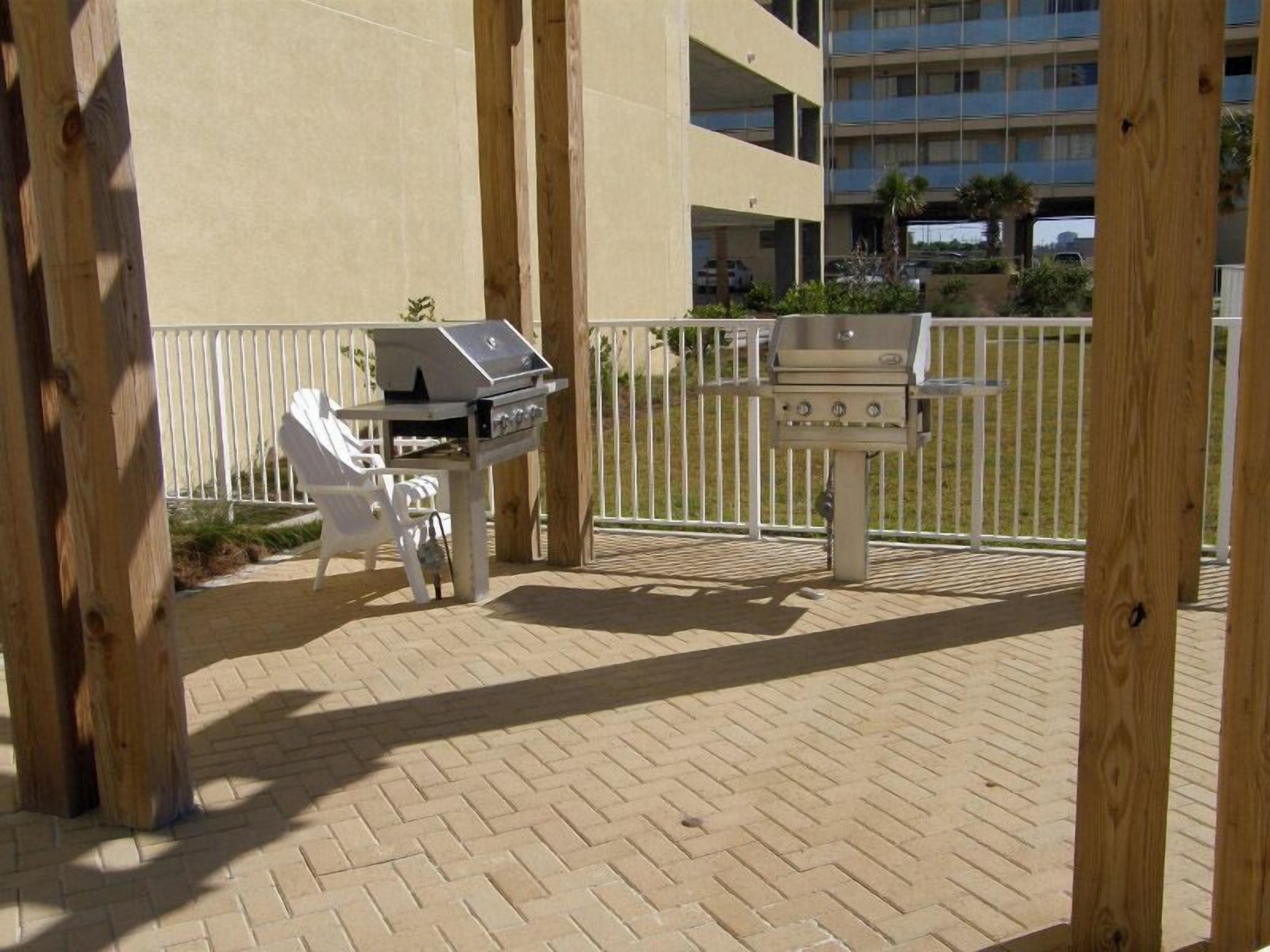 An outdoor barbecue area with two grills, surrounded by a wooden deck and a white fence.
