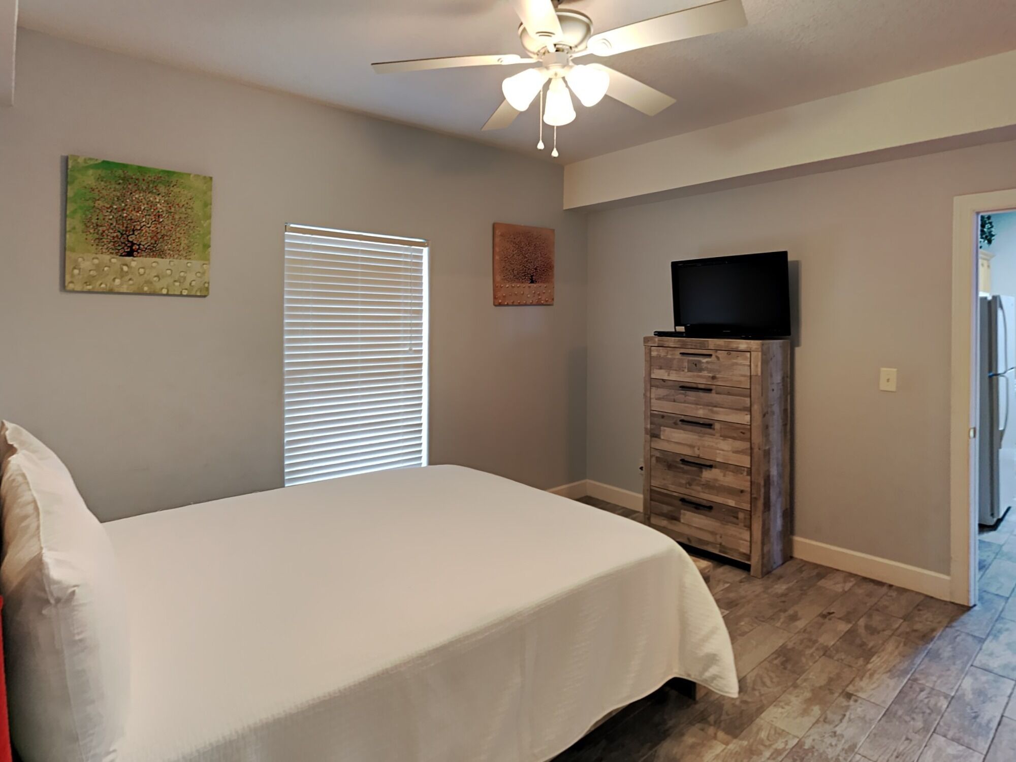 A bedroom with a bed, a ceiling fan, a dresser, and a television.