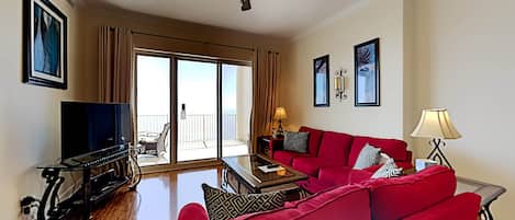 A living room with a red sofa, a TV, a ceiling fan, and a balcony with curtains.