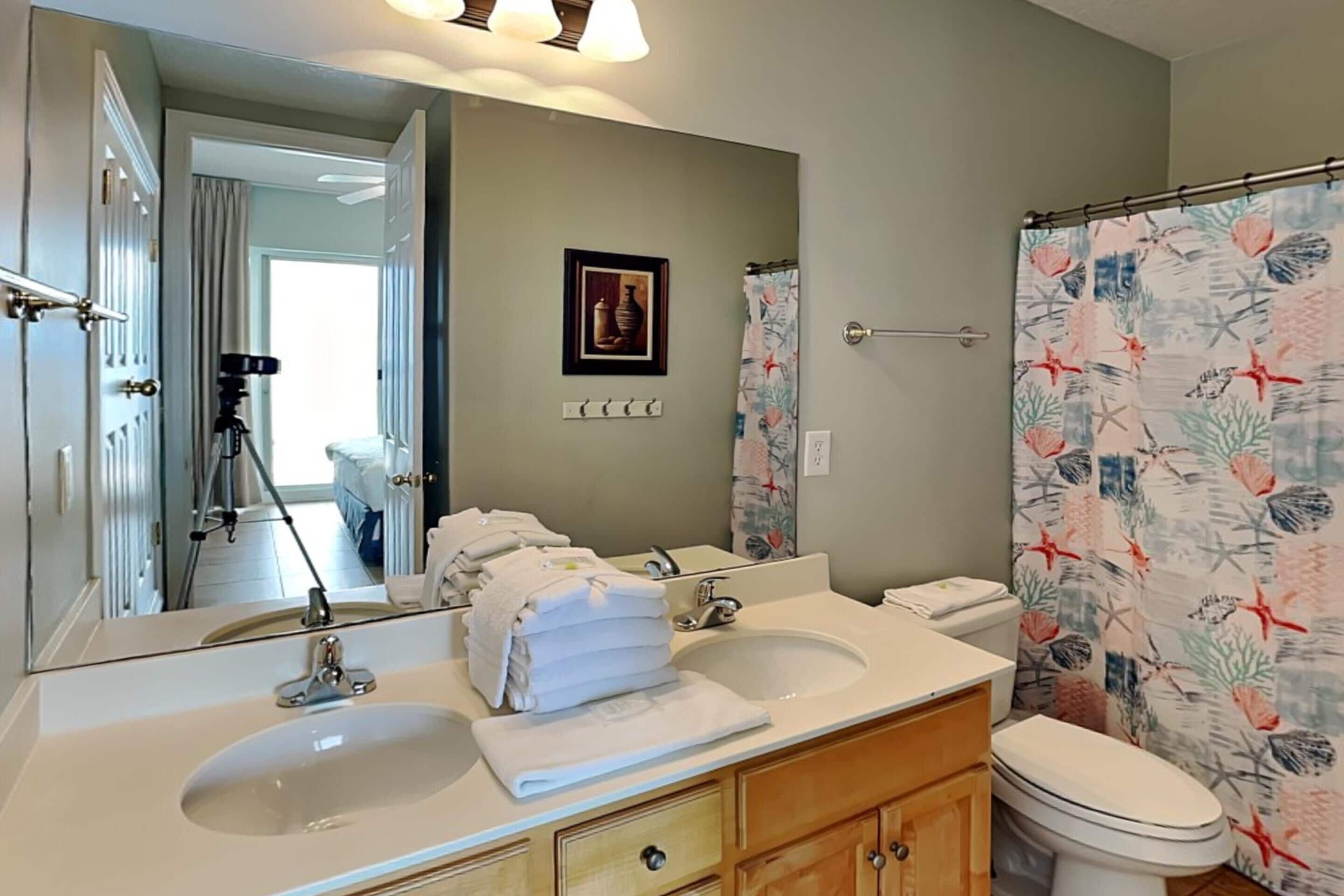 A bathroom with a double sink, a toilet, and a shower curtain with a floral pattern.