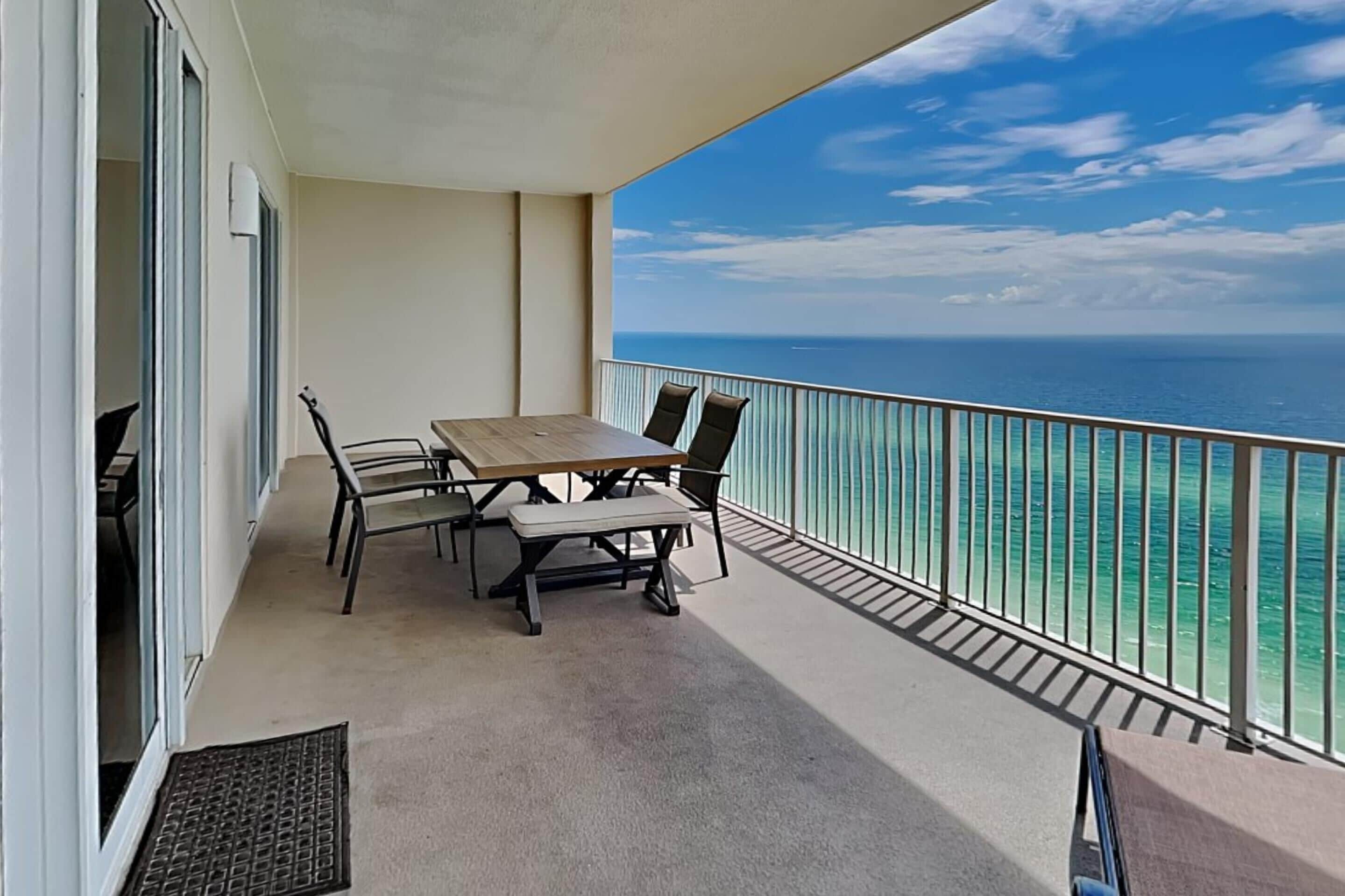 A balcony with a table and chairs, overlooking a clear blue sea.