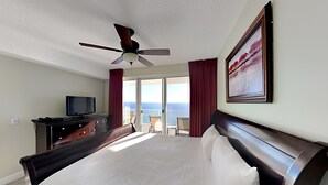 A hotel room with a large bed, a ceiling fan, a television on a dresser, and a balcony with a view of the ocean. - Ocean Reef by Resort Collection (Panama City Beach)