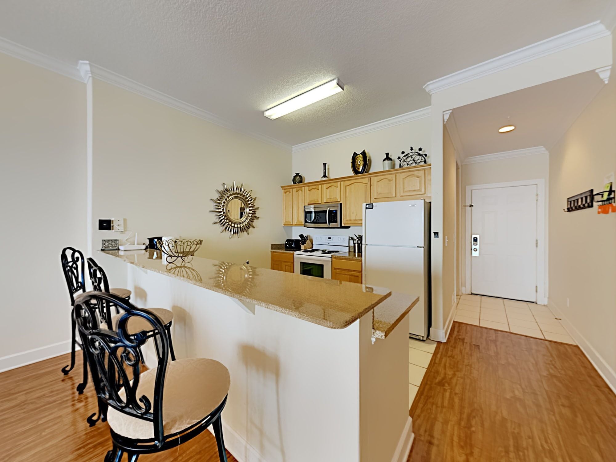 A kitchen with a central island, wooden cabinets, a microwave, and a refrigerator. There are two chairs and a decorative mirror on the wall.
