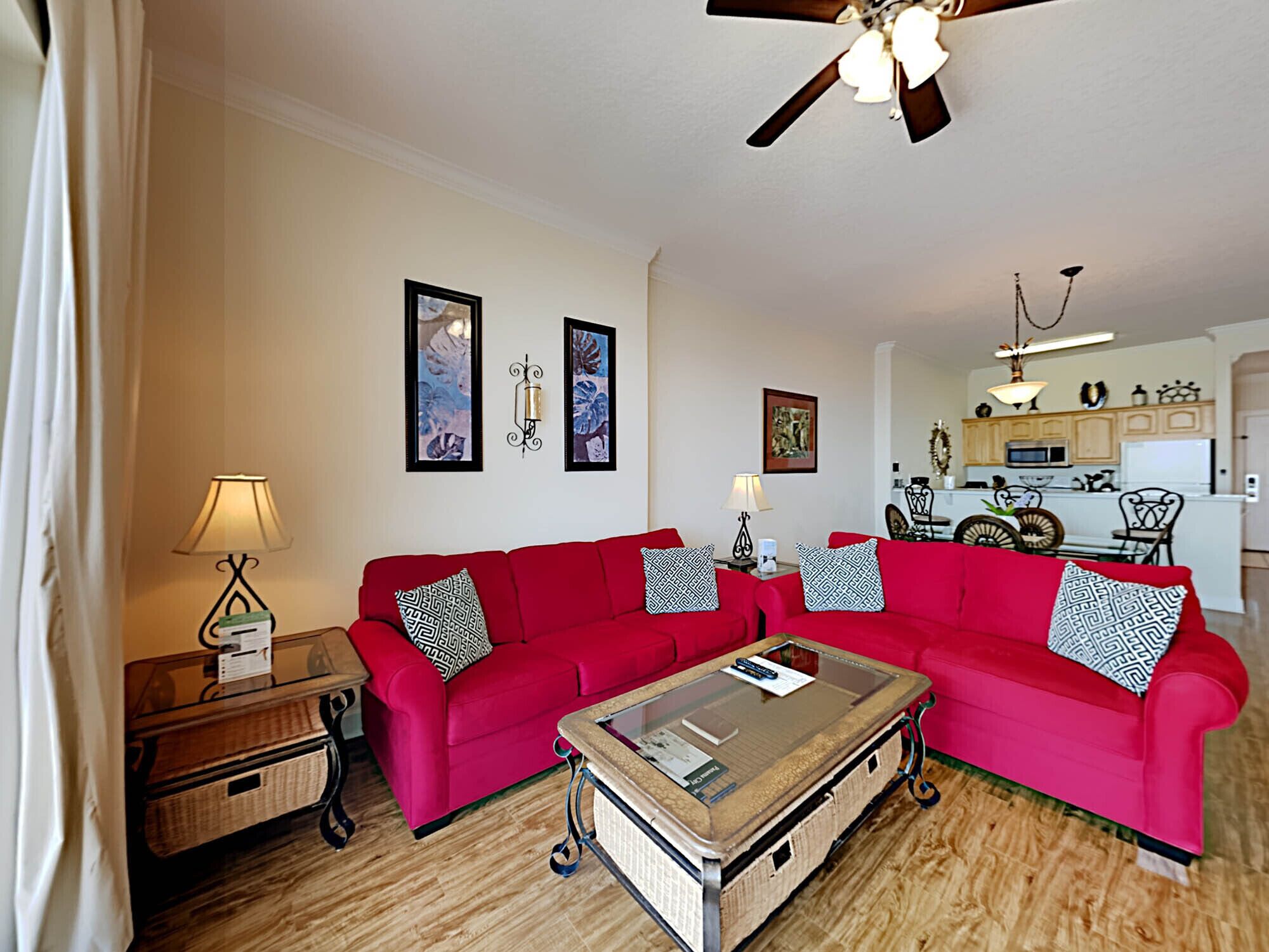 A living room with two red sofas, a glass coffee table, and a ceiling fan.