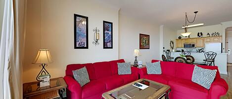 A living room with two red sofas, a glass coffee table, and a ceiling fan.