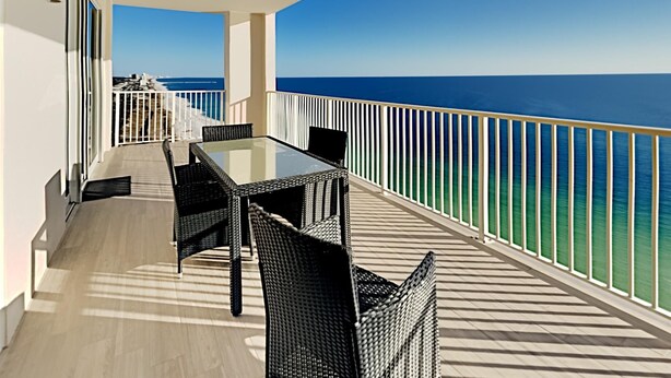 A balcony with a table and chairs, overlooking a clear blue sea. - Ocean Reef by Resort Collection (Panama City Beach)