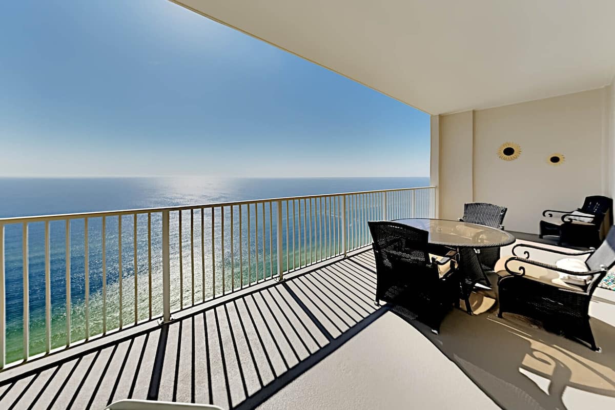 Een balkon met uitzicht op de oceaan, een tafel met stoelen en een zondecoratie aan de muur.