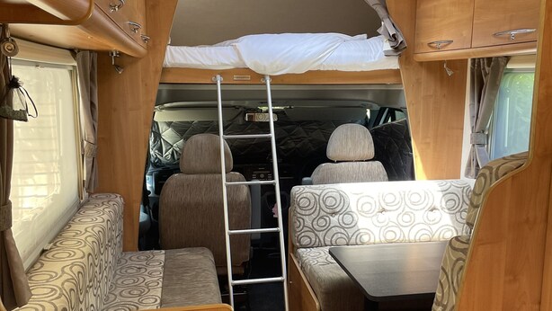 Interior compacto de autocaravana con kitchenette, zona de comedor y litera.