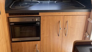 Una cocina compacta con ventanal sobre el fregadero, horno empotrado y muebles de madera.