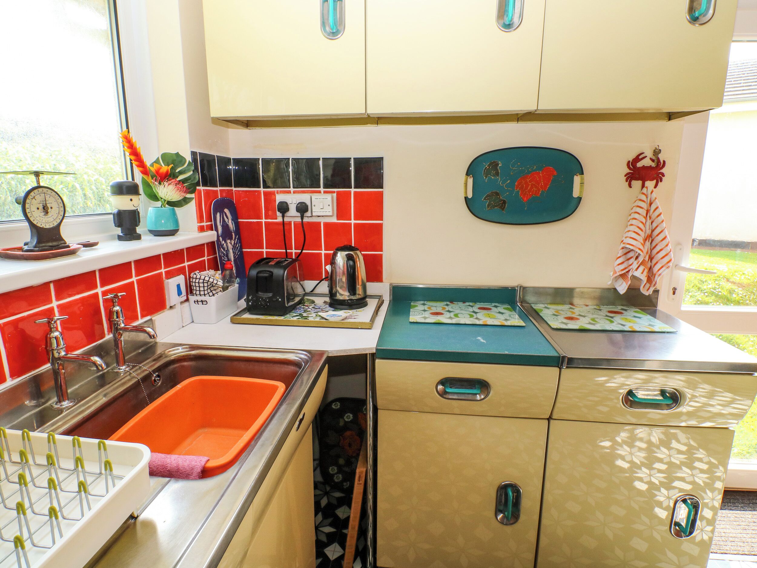 Eine Küche mit Spüle, Toaster und Wasserkocher auf der Arbeitsfläche. Es sind Schränke mit Griffen und ein Fenster über der Spüle vorhanden.
