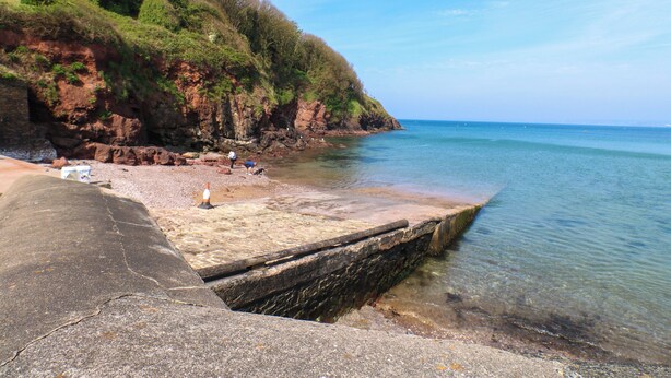 A coastal scene with a rocky cliff, clear blue sky, and calm sea. - Jasper's Corner (Kingsbridge)