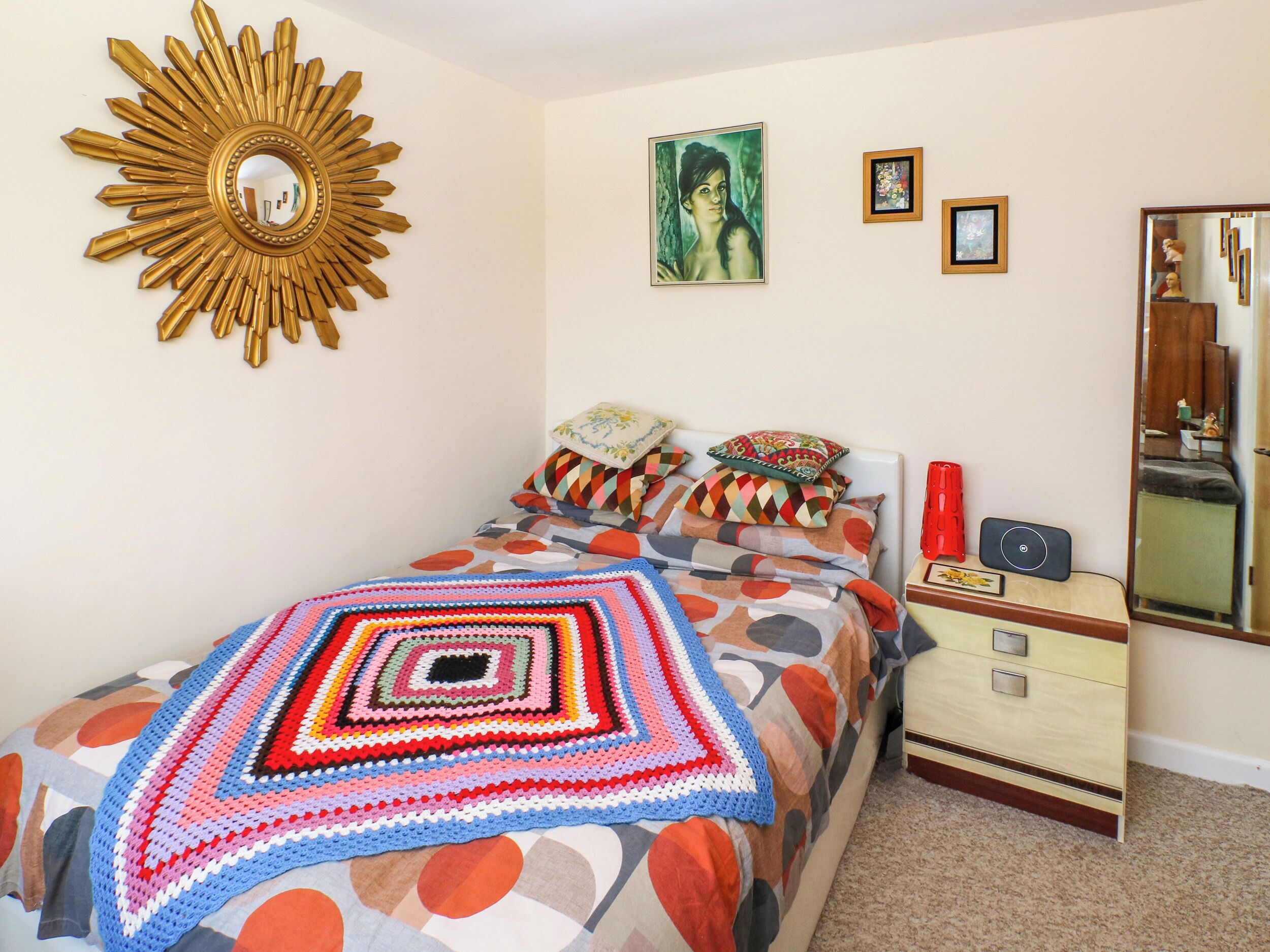 A bedroom with a bed, a nightstand, a dresser, a mirror, and wall art.