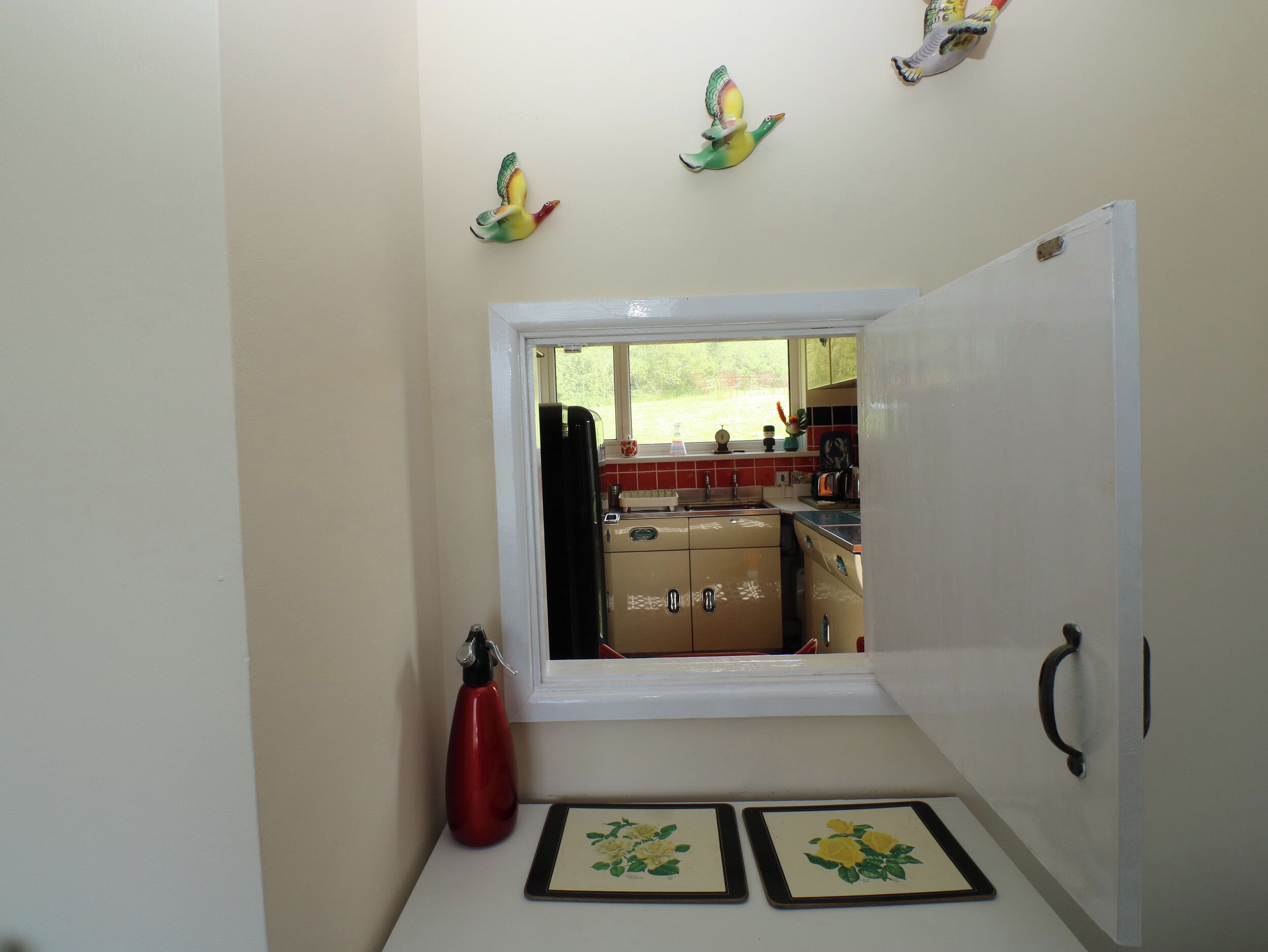 A narrow kitchen with a window, a red water bottle, and two framed pictures on the counter.