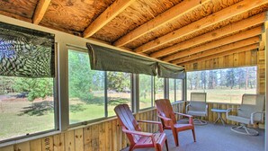 Ein Zimmer mit Holzwänden, großen Fenstern, zwei Adirondack-Stühlen und einem kleinen Tisch.