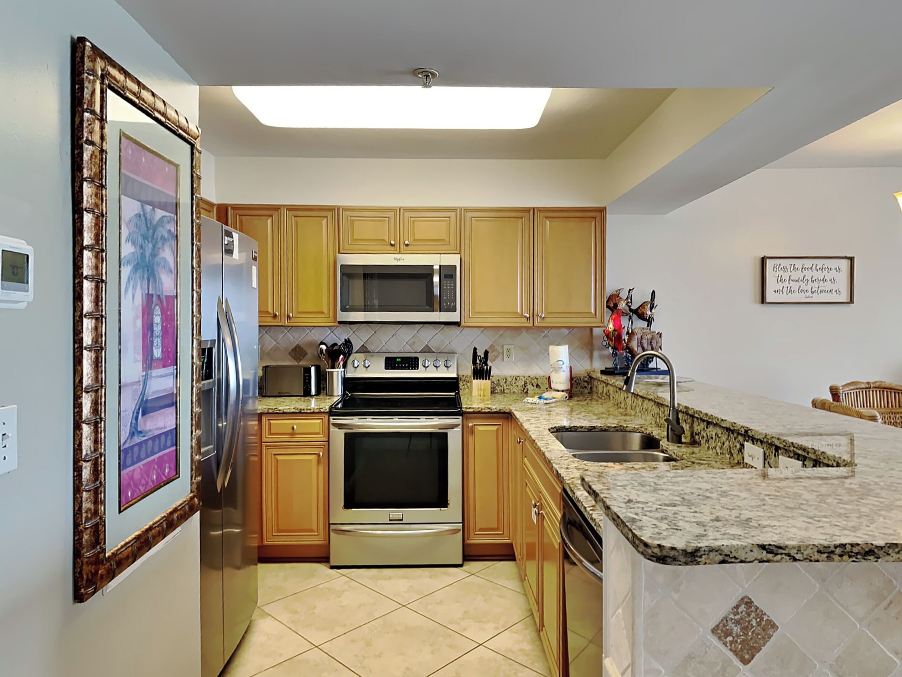 A kitchen with wooden cabinets, stainless steel appliances, a granite countertop, and a tiled floor.