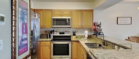 A kitchen with wooden cabinets, stainless steel appliances, a granite countertop, and a tiled floor.
