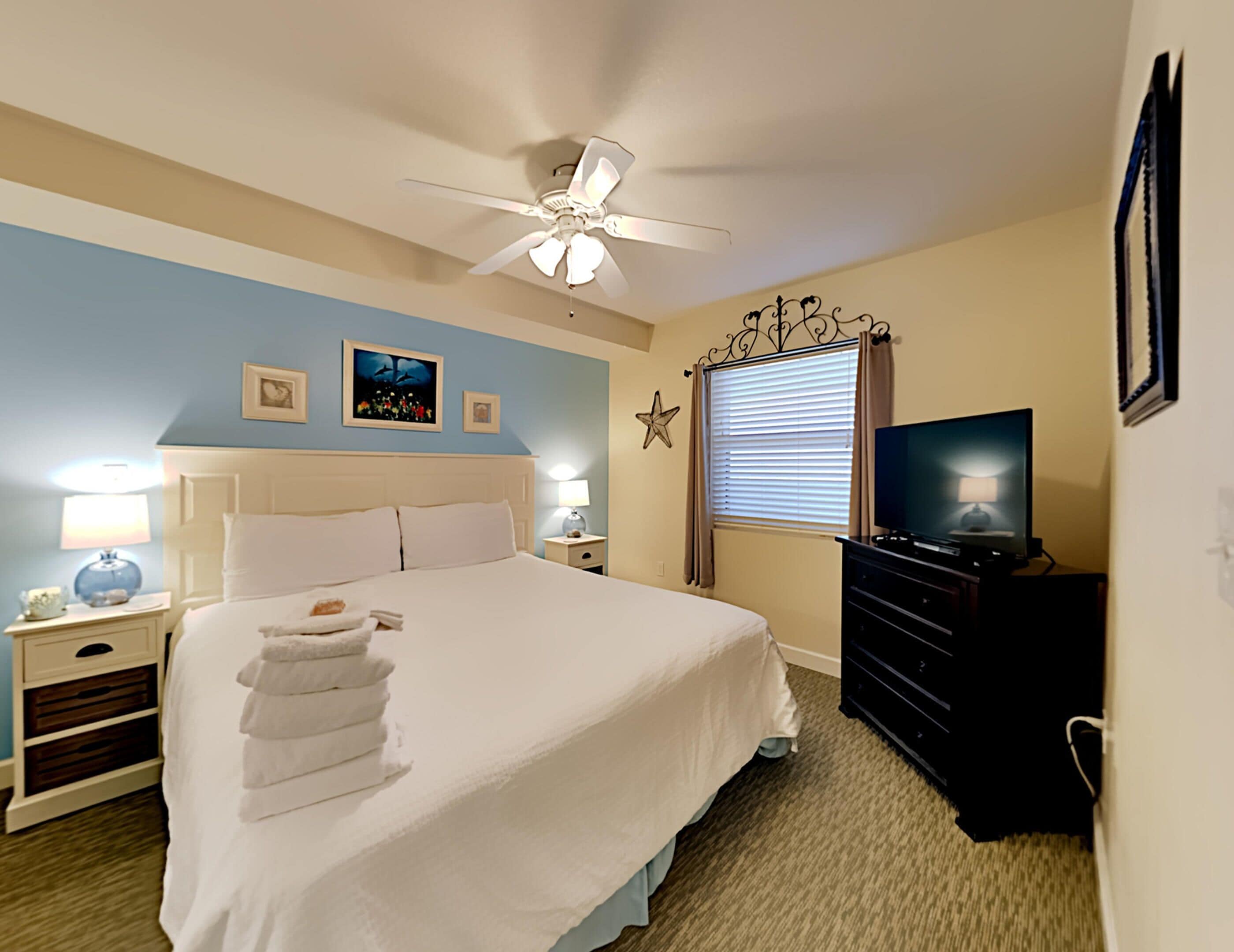 A neatly arranged hotel room with a bed, bedside lamps, a television, and a ceiling fan.